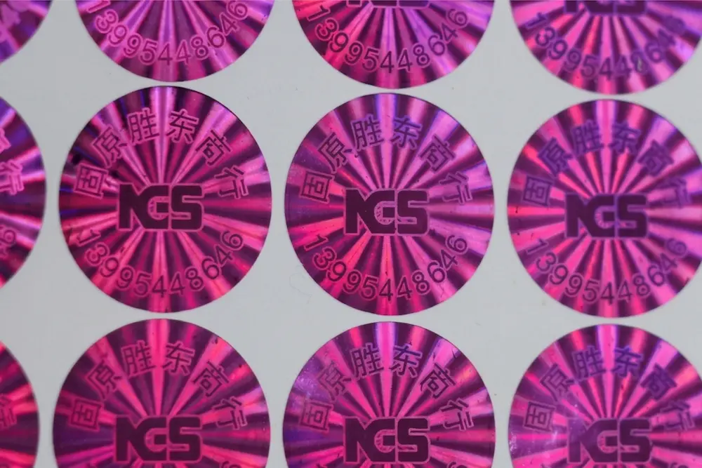 Custom magenta holographic security labels supplied on sheet backing with repeated serial-style label designs