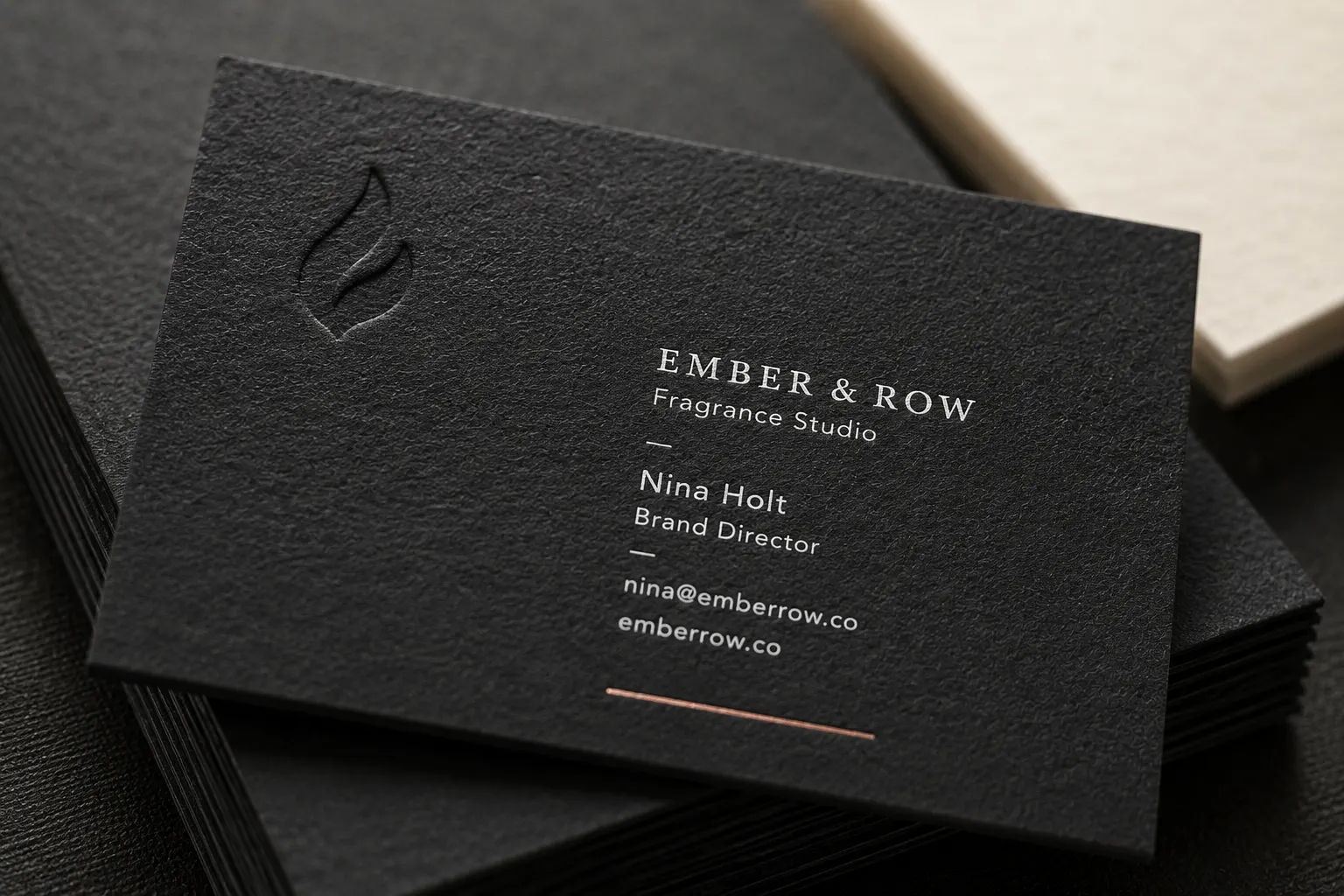 Close-up of black cotton paper business cards with visible uncoated texture, blind deboss mark and restrained white ink.