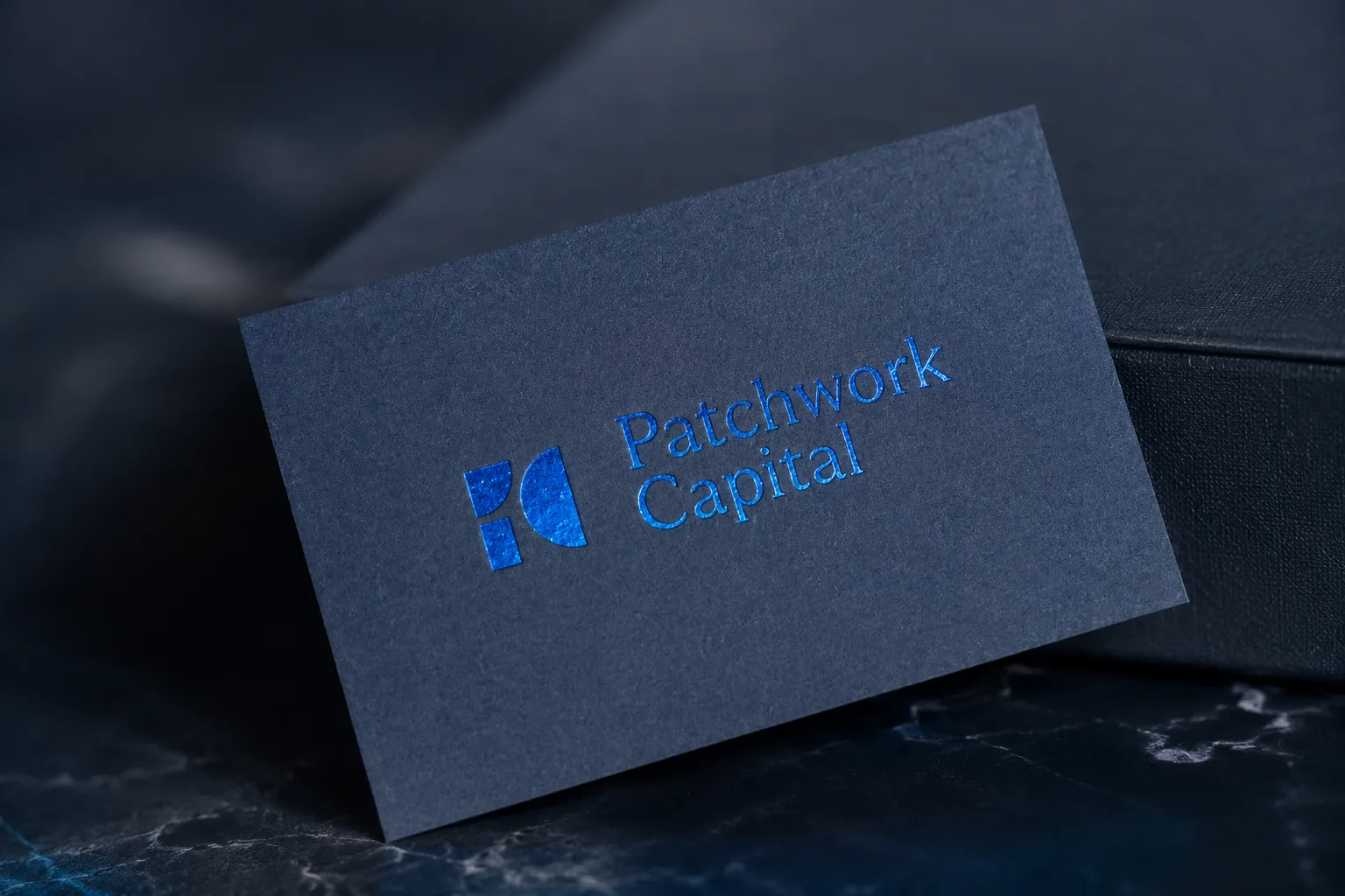 Dark blue business card with blue metallic foil logo and restrained premium typography.