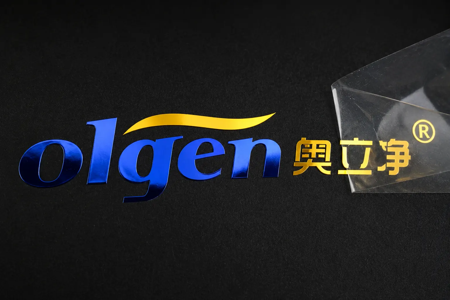 Blue and gold thin metal transfer logo applied to a black textured surface without visible sticker background