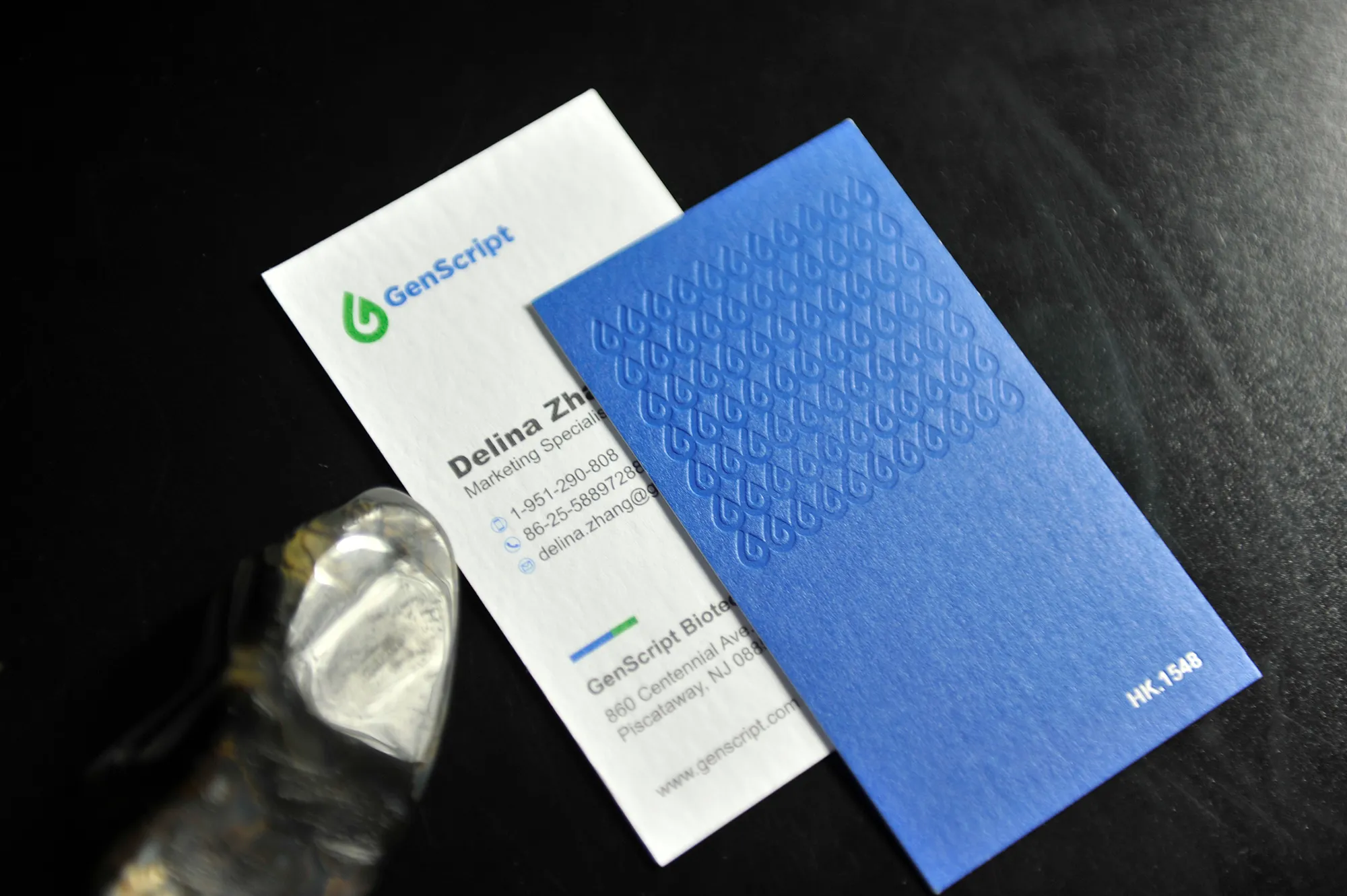 Blue business card with a repeating blind deboss logo pattern paired with a clean white contact card.