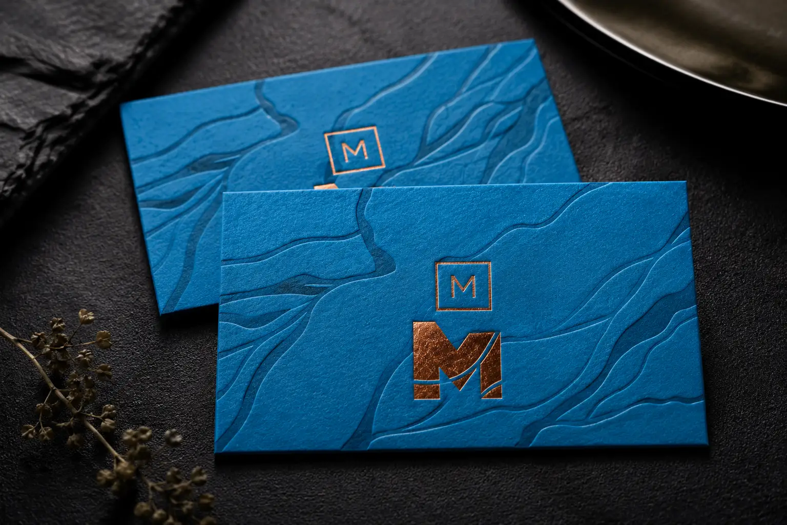 Blue premium business cards with copper foil monogram detail and textured foil-ready surface design.