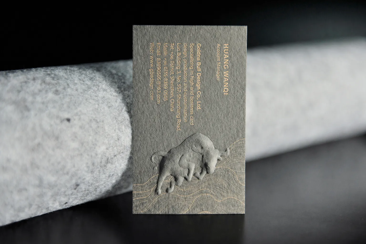 Grey business card sample with a sculpted raised emboss detail and muted premium paper surface.