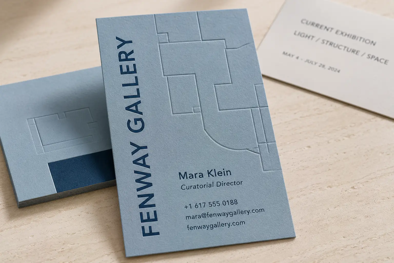 Light blue business card with subtle debossed geometric artwork and clean gallery contact details.