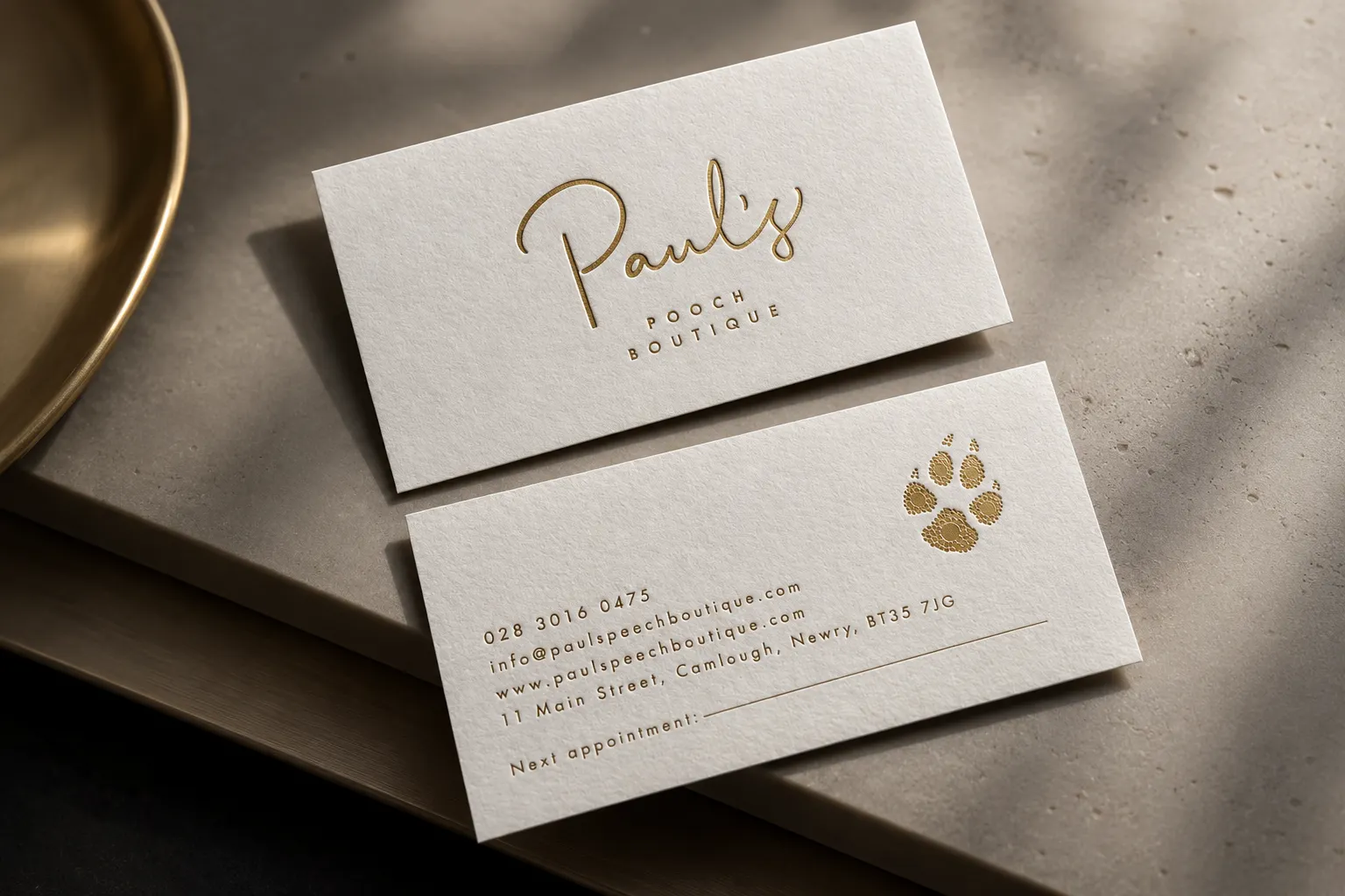 White business cards with gold foil script logo and small paw detail for a premium pet service brand.