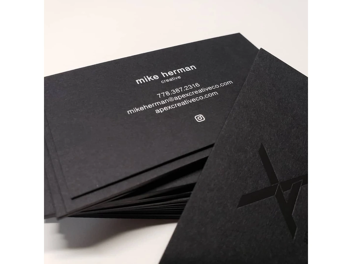 Stack of black cardstock business cards with white contact details and a black-on-black geometric mark.