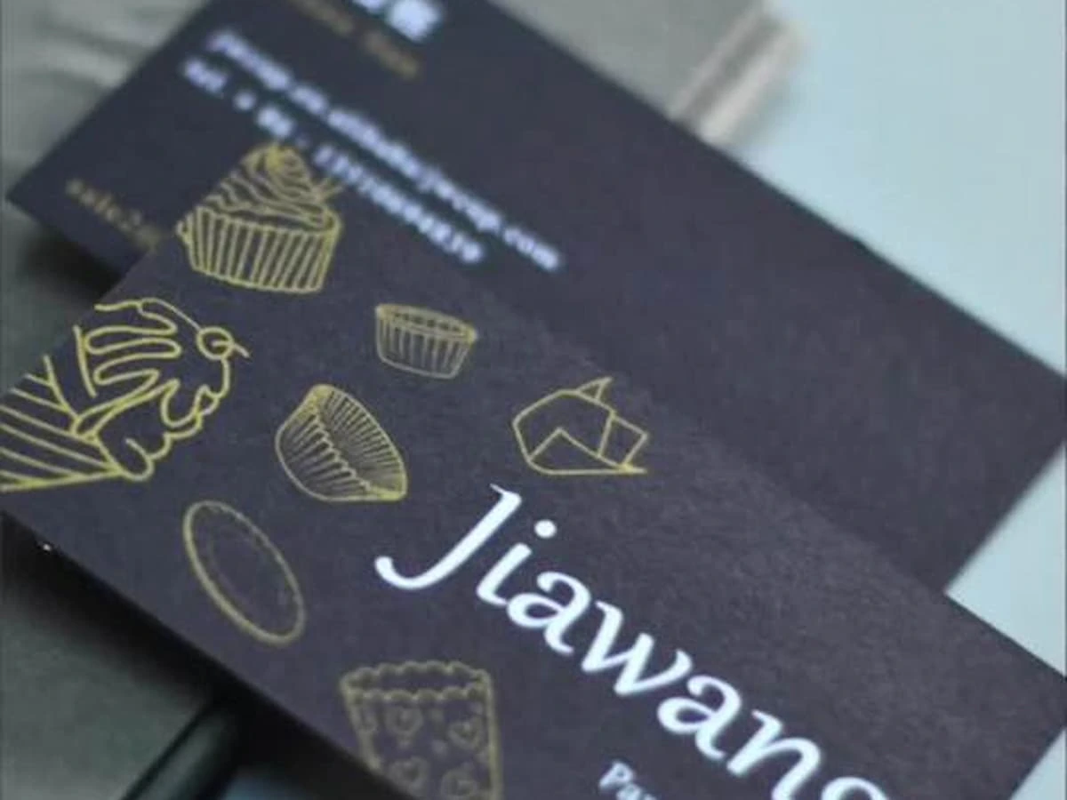 Close-up of a black cardstock business card with white lettering and gold line illustrations.