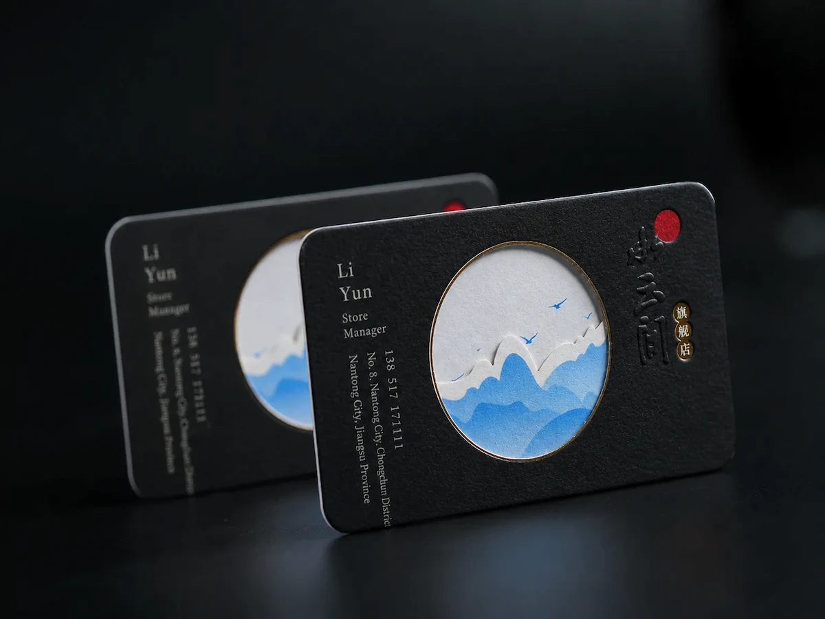 Two black business cards with circular windows showing blue and white landscape artwork