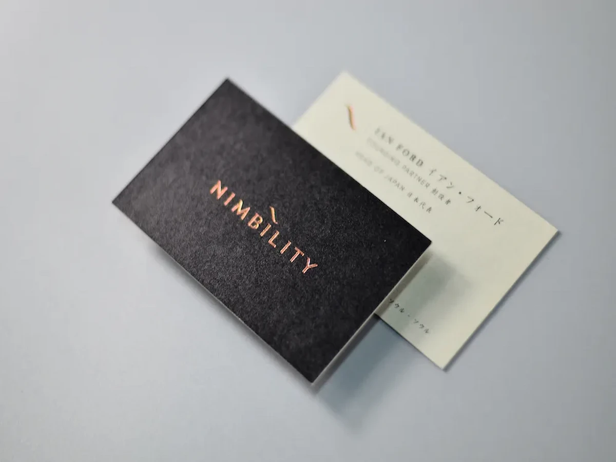 Black business card with reflective copper-colored lettering resting over a cream card