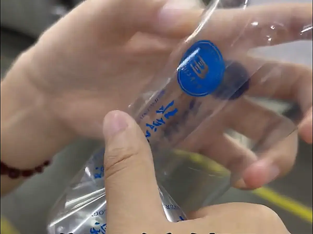 A thumb presses a clear label against a transparent bottle.