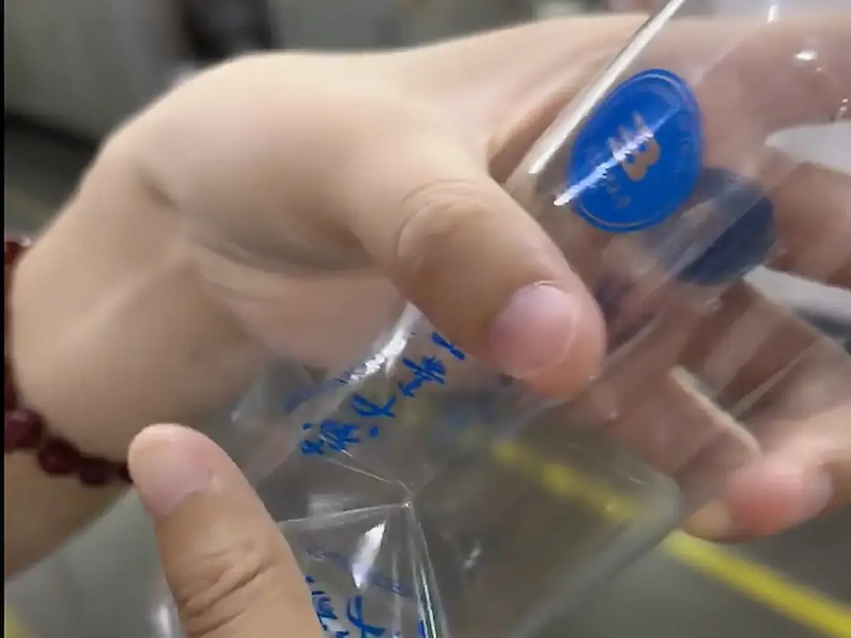 Hands smooth a clear label across a transparent bottle.