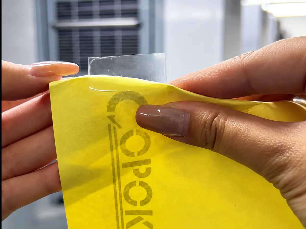 Hands lift a clear label while holding its yellow backing sheet.