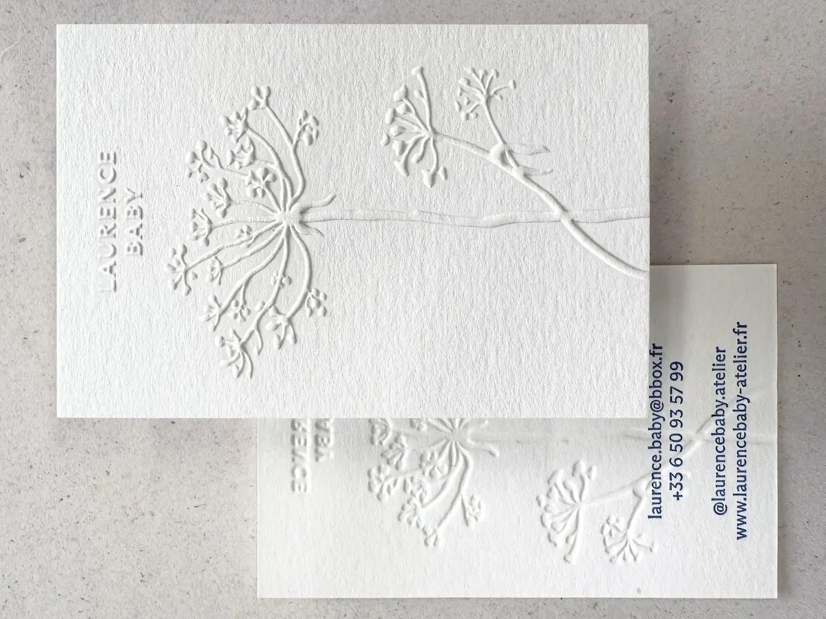 Two white textured business cards with raised floral embossing and blue contact details.