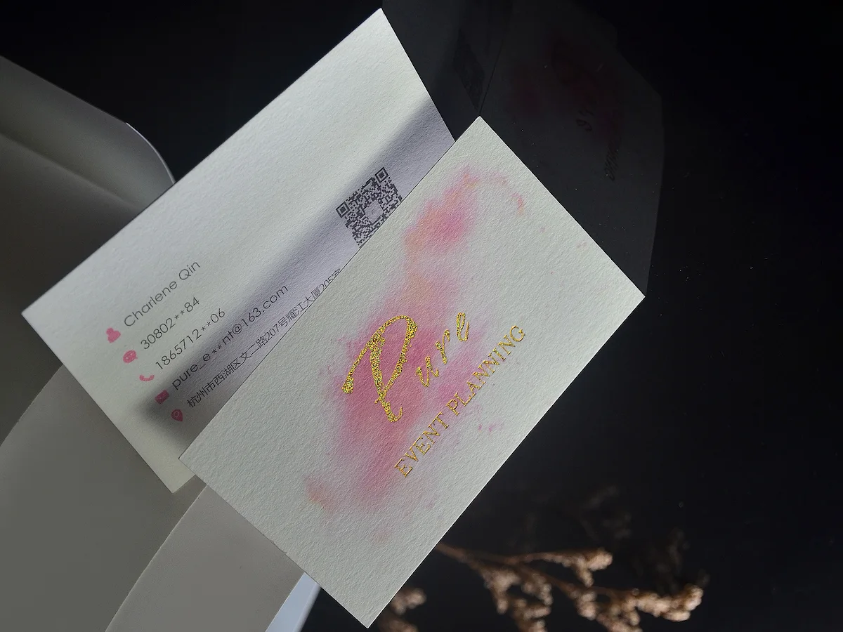 Two white textured cotton paper cards with pink print, gold foil lettering, and printed contact details.