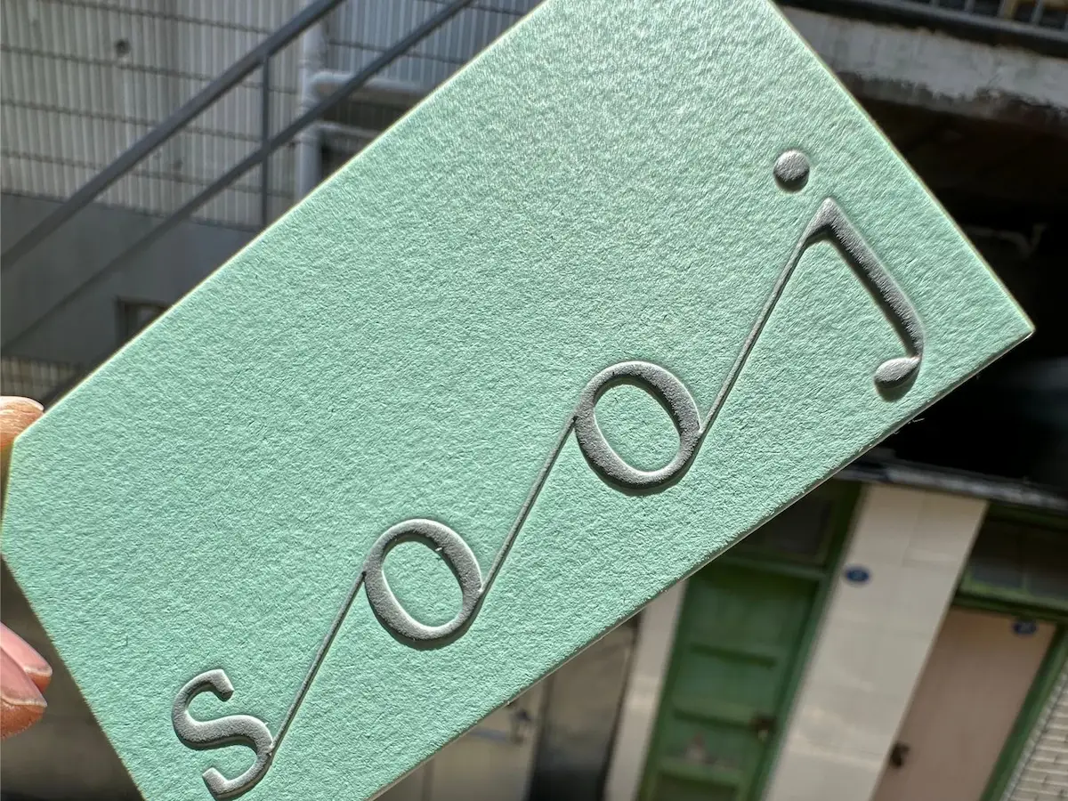 Mint-green cotton paper card with prominently raised embossed lettering.