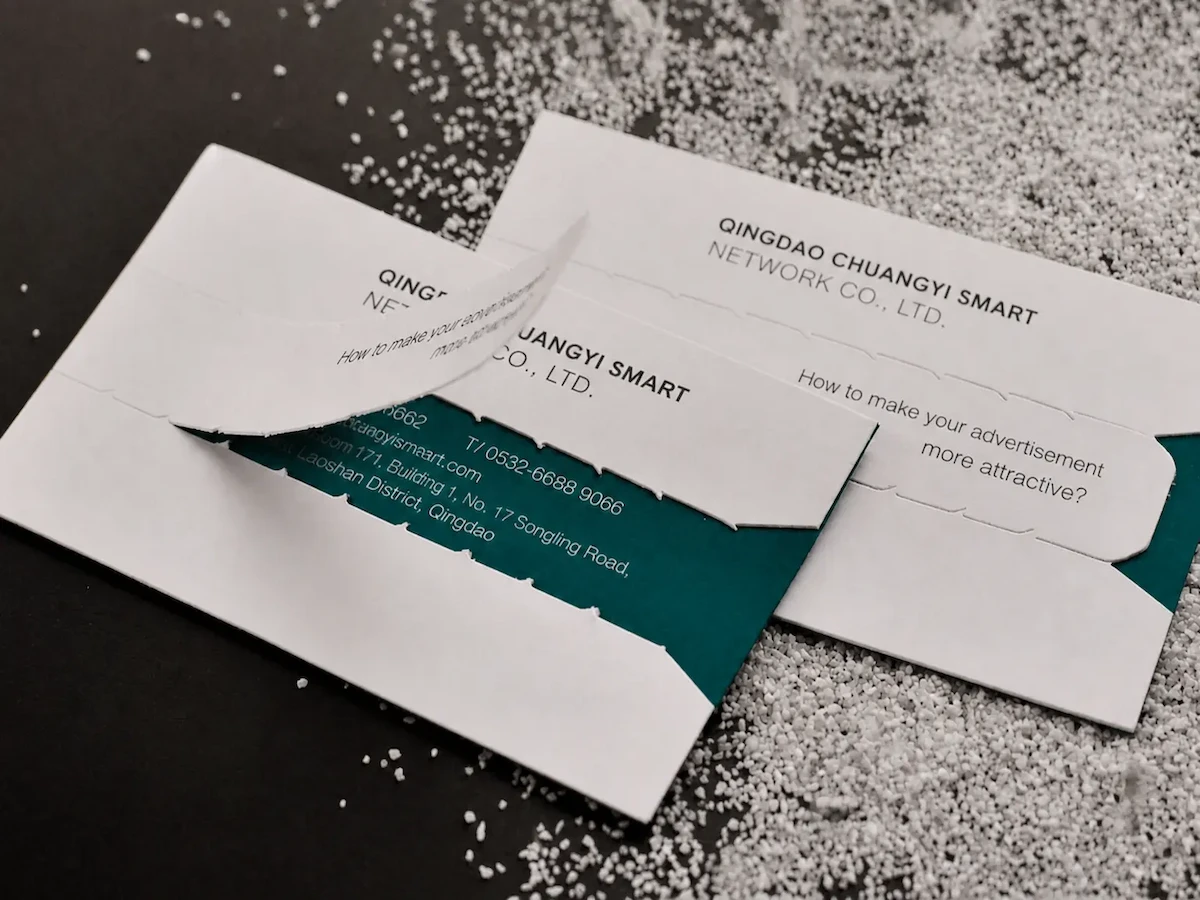 Two white business cards with tear-off panels revealing dark teal sections